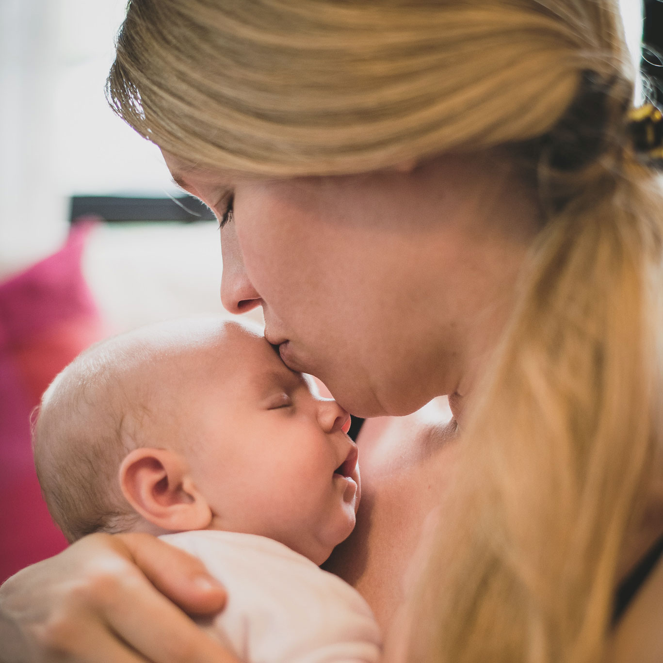A mother kissing her sleeping newborn on the forehead